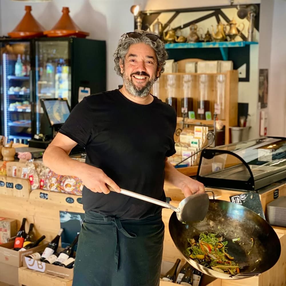 Le chef de COMBO souriant, wok en main, devant le comptoir de l'épicerie